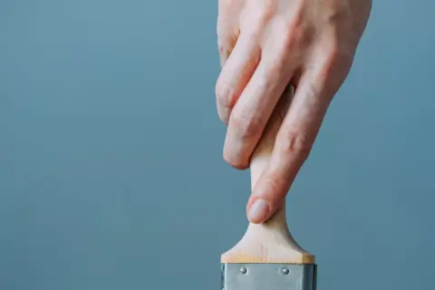 Mano che tiene un pennello, utile per capire come togliere lo smalto dai vestiti.