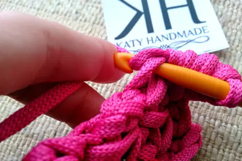 Mano che lavora all'uncinetto con filo rosa acceso, creando un punto pieno. Un tutorial su come ricamare una stella a punto pieno.