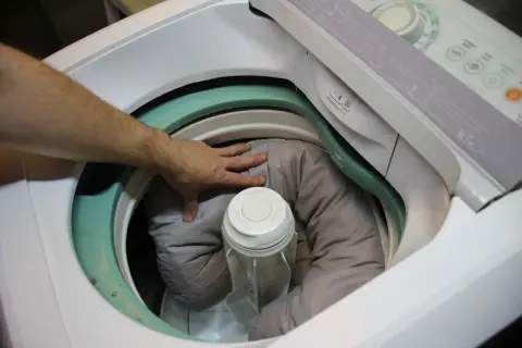 Mano che sistema la cuccia del cane nella lavatrice, pronta per essere lavata.