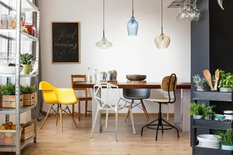 Tavola apparecchiata con lampadario decentrato soluzioni moderne. Sedie colorate e lavagna con scritta "Good morning".