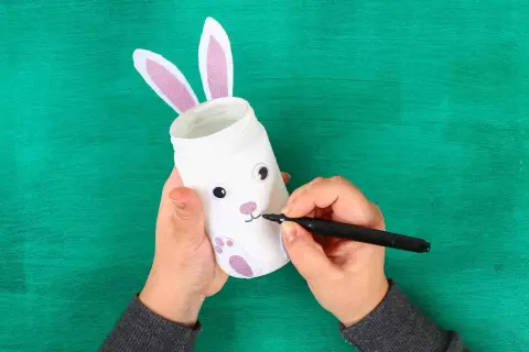 Mani che creano un coniglietto pasquale con un barattolo, perfetto per i lavoretti di Pasqua scuola infanzia.