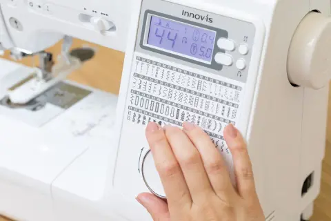 Dito, una mano seleziona tra i tanti punti macchina da cucire disponibili su un display digitale.