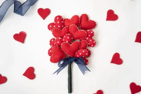 Un bouquet di cuori rossi in feltro, perfetti per regali fai da te San Valentino. Un nastro blu lega il tutto, circondato da cuoricini sparsi.
