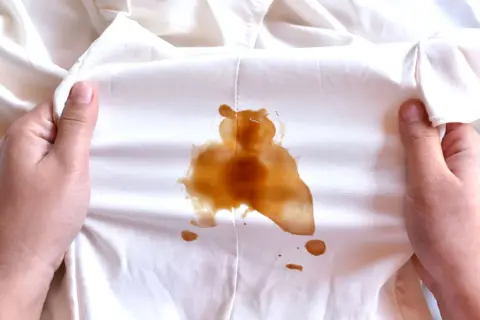 Mani che mostrano macchie di sapone marroni su un tessuto bianco.