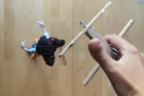 Mano che muove un marionette fai da te con fili di controllo in legno.