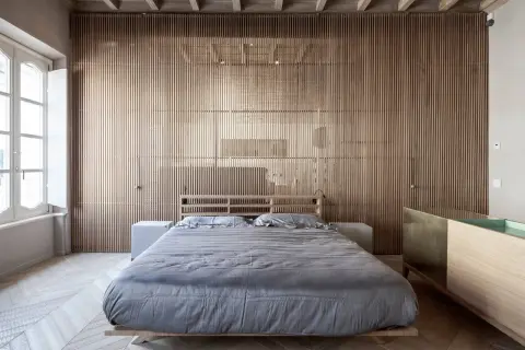 Camera da letto in stile giapponese con pareti in listelli di legno, letto basso con lenzuola grigie e un mobile in legno e ottone.