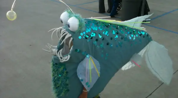 Un bambino indossa un costume da pesce lanterna fai da te, perfetto per un tema mare. Le paillettes blu e la canna da pesca con la luce lo rendono unico.