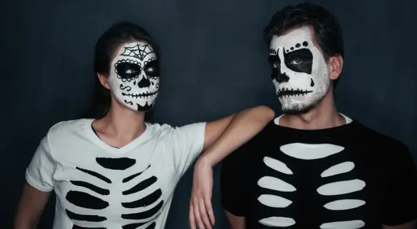 Coppia con trucco da teschio e magliette fai da te a tema scheletro, perfetti per costumi Halloween uomo e donna.