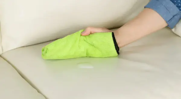 Mano che pulisce una macchia di liquido su un divano chiaro con un panno verde. La birra macchia i vestiti, ma questo panno è pronto a salvare il divano.