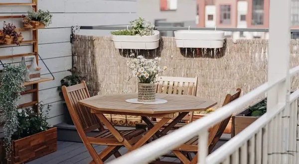 Un tavolo e sedie in legno per arredare balcone piccolo. Piante in vaso e decorazioni creano un angolo accogliente.