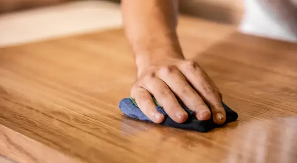 Mano che lucida un mobile in legno. Scopri come togliere graffi dai mobili laccati con cura e pazienza.