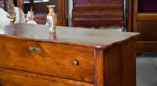 Cassettiera in legno scuro, oggetto di **ristrutturazione mobili antichi**, con vaso decorato e modellini di navi sullo sfondo.