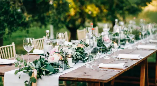 Tavola apparecchiata all'aperto con fiori, candele e bicchieri. Un'idea per le decorazioni matrimonio fai da te.