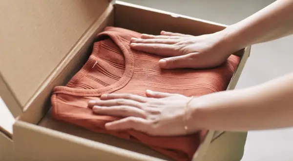 Mani che accarezzano una maglietta color terracotta appena arrivata, pronta per il primo lavaggio per fissare i colori.