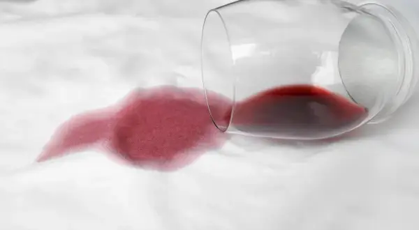 Calice di vino rosso rovesciato su tessuto bianco, creando una macchia. Come togliere macchie sconosciute e ostinate.