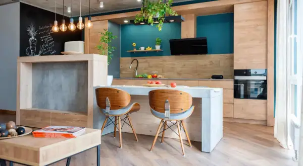 Cucina moderna con isola centrale e sedie in legno. L'arredamento mix and match crea un ambiente accogliente, con dettagli industriali e tocchi di colore vivace.