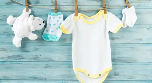Vestiti da neonato bianchi e gialli appesi ad asciugare. Scopri come smacchiare i vestiti dei neonati ingialliti per mantenerli freschi.