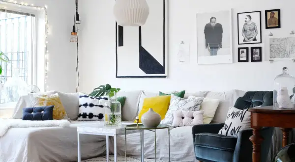 Un accogliente soggiorno fai da te con divano bianco, cuscini colorati e stampe artistiche alle pareti.