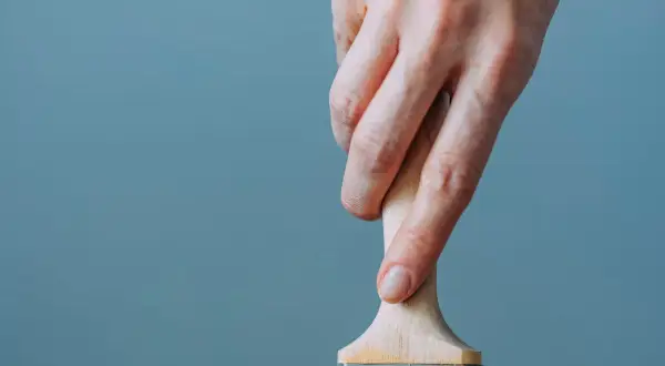 Mano che tiene un pennello, utile per capire come togliere lo smalto dai vestiti.