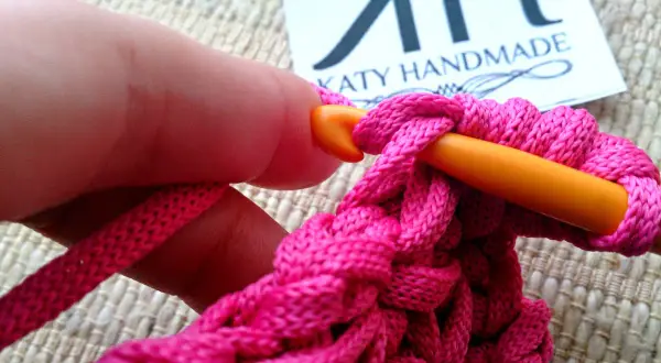 Mano che lavora all'uncinetto con filo rosa acceso, creando un punto pieno. Un tutorial su come ricamare una stella a punto pieno.