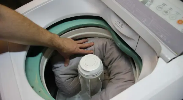 Mano che sistema la cuccia del cane nella lavatrice, pronta per essere lavata.