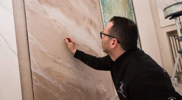 Artista crea effetti materici su pannello, mostrando diversi tipi di pittura per interni.