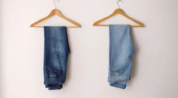 Due paia di jeans appesi: uno scuro, l'altro chiaro. Scopri come scolorire i jeans senza candeggina per ottenere questo effetto.