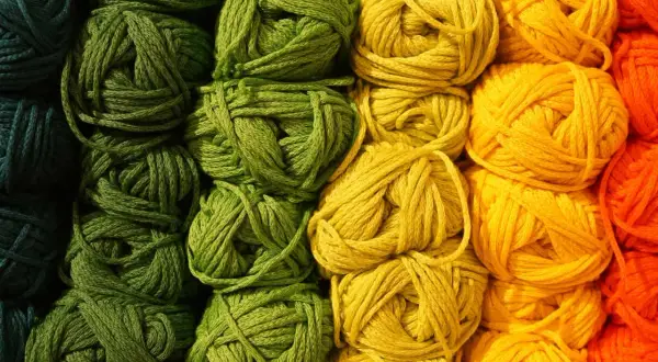 Gomitoli di lana colorata, con un'abbondanza di macchie gialle che si fondono con il verde e l'arancione, pronti per un progetto creativo.