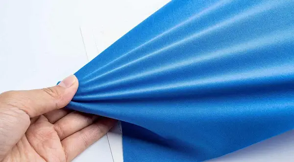 Mano che tiene un tessuto blu brillante, mostrando la sua elasticità e la trama del punto elastico a mano.