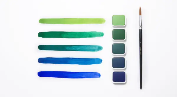 Pennellate verdi e blu mostrano la differenza tra colori acrilici e tempere, con pastiglie di colore e un pennello.