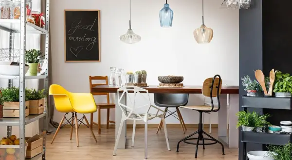 Tavola apparecchiata con lampadario decentrato soluzioni moderne. Sedie colorate e lavagna con scritta "Good morning".