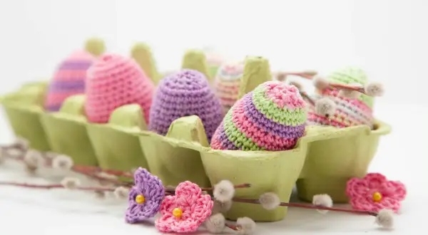 Uova di Pasqua all'uncinetto in lana colorata, perfette per lavoretti di Pasqua creativi. Fiori e ramoscelli di salice completano la scena.