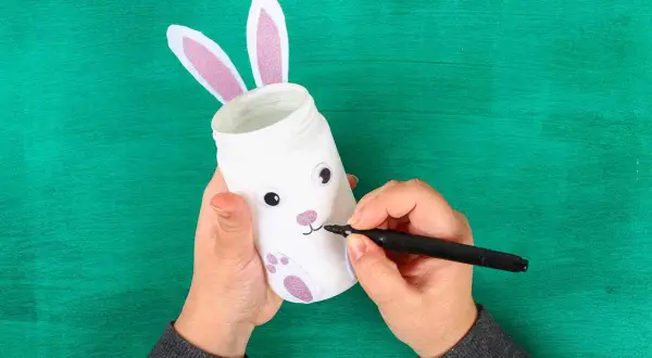 Mani che creano un coniglietto pasquale con un barattolo, perfetto per i lavoretti di Pasqua scuola infanzia.
