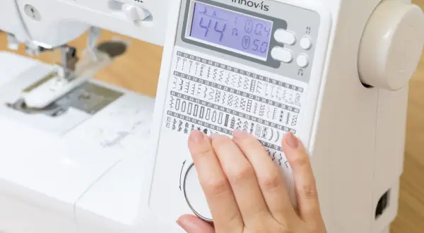 Dito, una mano seleziona tra i tanti punti macchina da cucire disponibili su un display digitale.