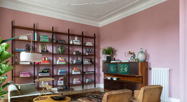 Soggiorno accogliente con **caldi colori pareti** rosa cipria, libreria a giorno piena di libri e oggetti, divano verde, poltrone in pelle e mobile vintage.