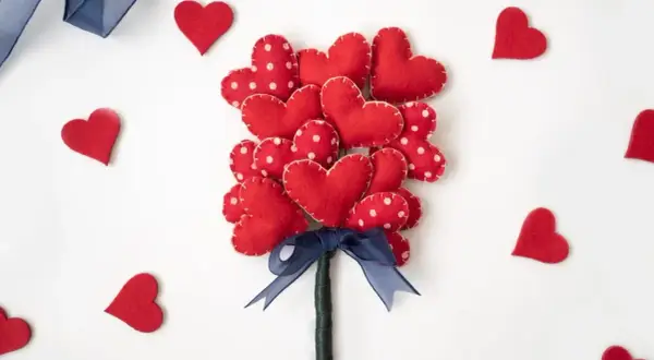 Un bouquet di cuori rossi in feltro, perfetti per regali fai da te San Valentino. Un nastro blu lega il tutto, circondato da cuoricini sparsi.