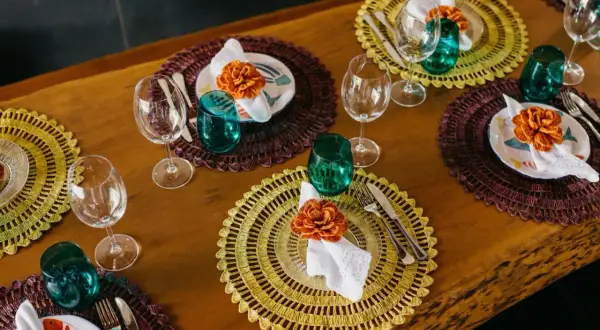 Sottopiatti eleganti fai da te con decorazioni floreali arancioni, bicchieri verdi e posate su un tavolo di legno.