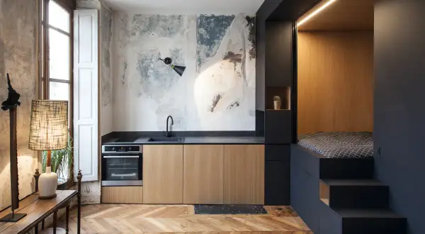 Cucina moderna con letto a soppalco, un esempio di idee arredo casa piccola. Pareti grezze, mobili in legno e dettagli industriali.