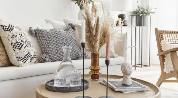 Tavolino rotondo con decanter, bicchieri, candele e scultura di testa. Cuscini decorativi e pampas sul divano creano un'atmosfera boho chic arredamento.