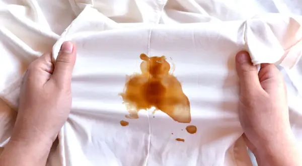 Mani che mostrano macchie di sapone marroni su un tessuto bianco.