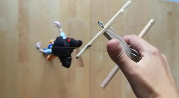 Mano che muove un marionette fai da te con fili di controllo in legno.