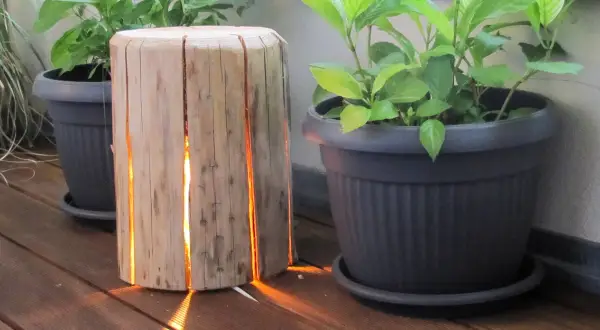 Lampada tronco legno fai da te illumina con calore il deck, creando un'atmosfera accogliente tra le piante in vaso.
