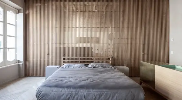 Camera da letto in stile giapponese con pareti in listelli di legno, letto basso con lenzuola grigie e un mobile in legno e ottone.