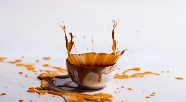 Schizzo di liquido marrone da una ciotola, creando macchie arancioni sui vestiti e sul tavolo.