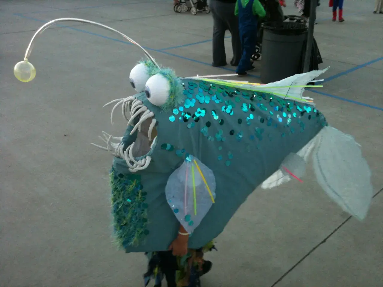 Un bambino indossa un costume da pesce lanterna fai da te, perfetto per un tema mare. Le paillettes blu e la canna da pesca con la luce lo rendono unico.