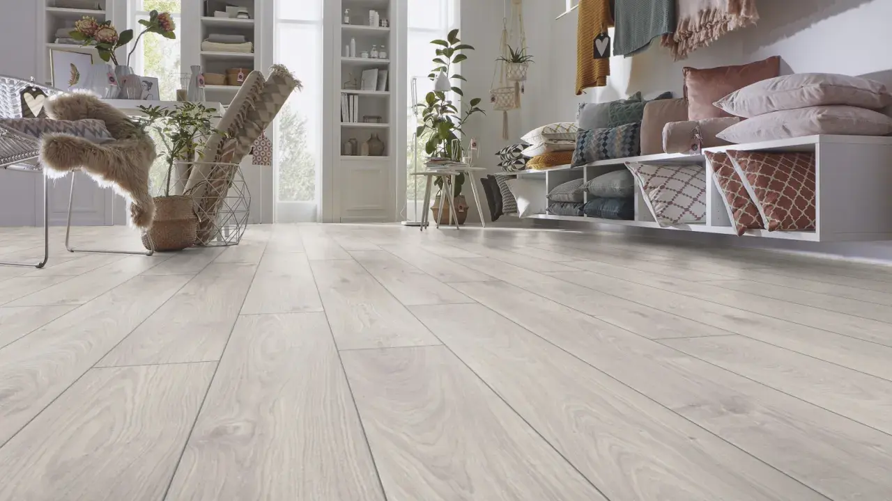 Un luminoso soggiorno con pavimento laminato effetto legno chiaro. Un divano con cuscini colorati e una libreria completano l'arredamento.