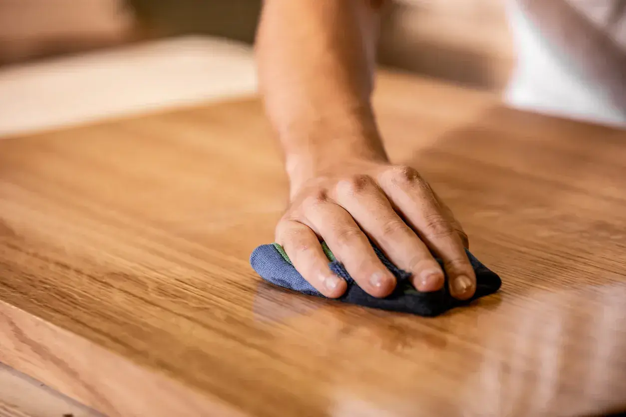 Mano che lucida un mobile in legno. Scopri come togliere graffi dai mobili laccati con cura e pazienza.