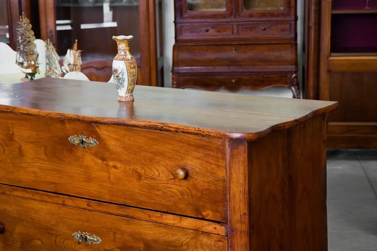 Cassettiera in legno scuro, oggetto di **ristrutturazione mobili antichi**, con vaso decorato e modellini di navi sullo sfondo.