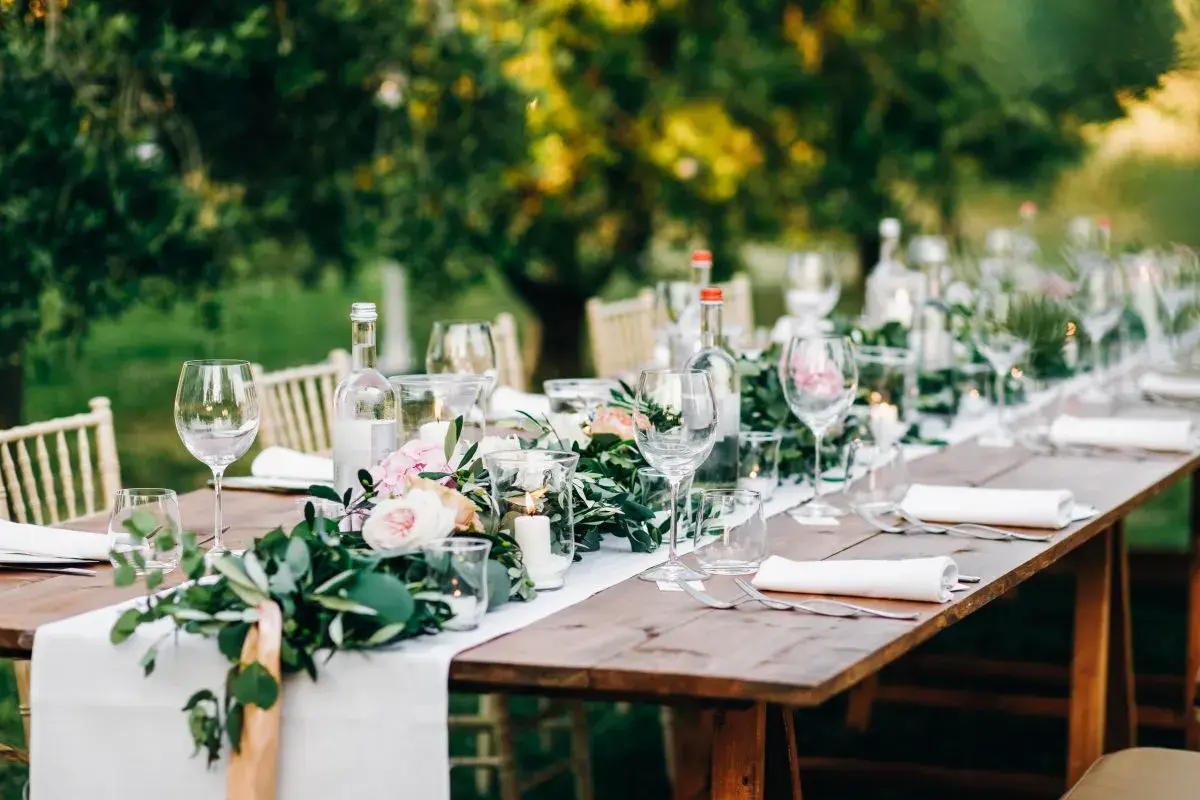 Tavola apparecchiata all'aperto con fiori, candele e bicchieri. Un'idea per le decorazioni matrimonio fai da te.