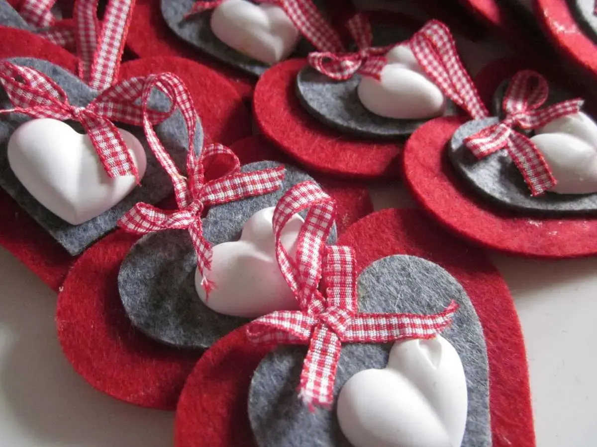 Cuori natalizi fai da te con feltro rosso e grigio, cuori bianchi e nastri a quadretti rossi.